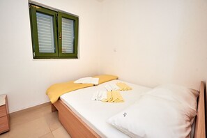 A small, clean room with a bed, a nightstand, and a window with green shutters. - Apartments Sea Front (Slivno)