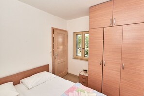 A bedroom with a bed, a wardrobe, a window, and a small table with a plant. - Apartments Sea Front (Slivno)
