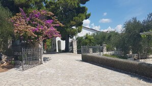 A paved pathway leading to a building with a stone wall and a metal gate. - Apartments Sea Front (Slivno)