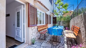 Un patio con tavolo e panche, pavimento in pietra e una porta con persiane.