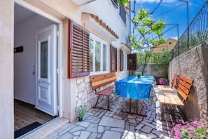 A patio with a table and benches, stone flooring, and a door with shutters. - Apartment Mici 1 (Cres)