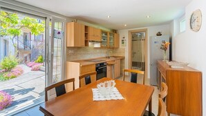 Una cucina moderna con mobili in legno, un tavolo da pranzo con sedie e vista su un giardino attraverso ampie finestre.