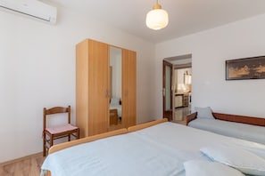 A bedroom with two beds, a wooden wardrobe, a chair, and a painting on the wall. - Apartment Mici 1 (Cres)