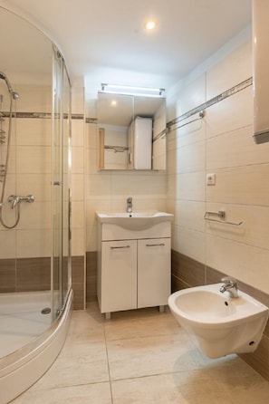 A modern bathroom with a glass-enclosed shower, a white sink, and a bidet. - Apartment Mici 1 (Cres)