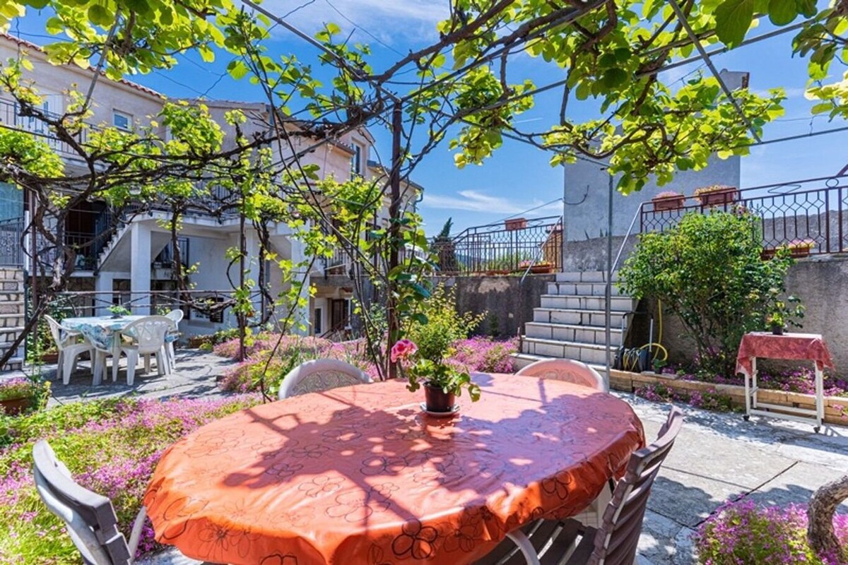 A patio with a table and chairs, surrounded by flowering plants and a view of buildings.