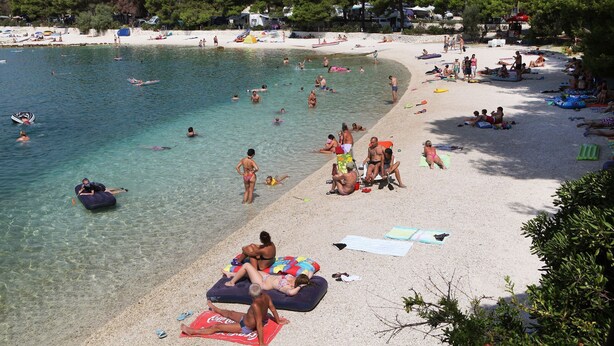 A beach with clear water, people swimming and sunbathing, and beach umbrellas. - Apartments Tereza (Trogir)