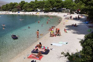 A beach with clear water, people swimming and sunbathing, and beach chairs and umbrellas. - Apartments Tereza (Trogir)