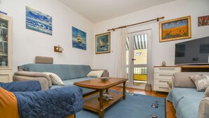 A living room with a sofa, a coffee table, and a TV. There are paintings on the wall and a window with curtains. - Apartments Tereza (Trogir)