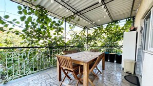 A covered patio with a wooden table and chairs, surrounded by a metal railing and potted plants. - Apartments Tereza (Trogir)