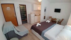Ein Hotelzimmer mit Bett, kleinem Schreibtisch mit Stuhl, Fernseher und einer kitchenette im Hintergrund.