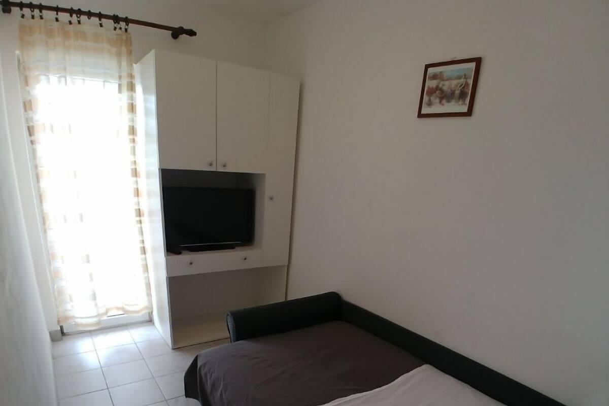 Une chambre à coucher avec un lit, un téléviseur fixé au mur et une fenêtre avec des rideaux.