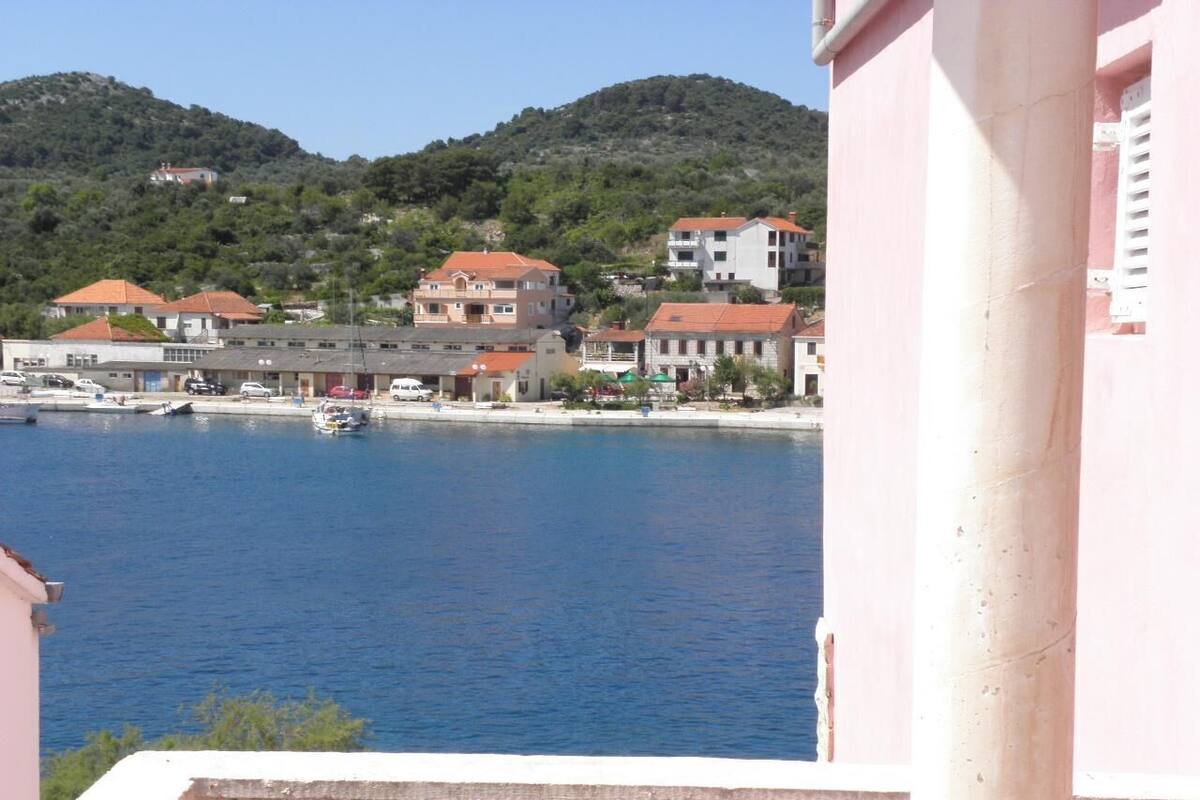 Une ville côtière avec des bâtiments qui bordent le front de mer, une mer bleue et limpide, et des collines en arrière-plan.