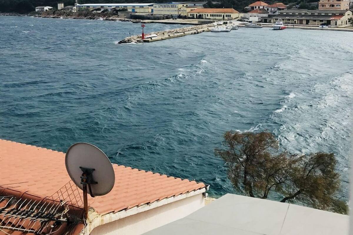 Une vue côtière avec une antenne parabolique sur le toit d’un immeuble, une jetée s’avançant dans l’eau et une colline en arrière-plan.