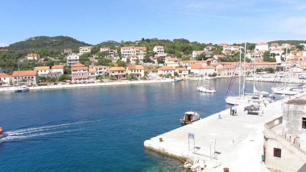 Eine Küstenstadt mit einer Marina, klarem blauen Wasser und Häusern mit roten Dächern.