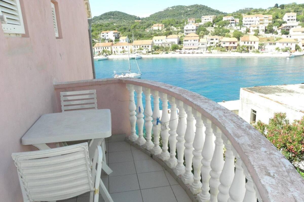 Un balcon avec une table et une chaise blanches, donnant sur une ville côtière avec ses bâtiments et ses bateaux.
