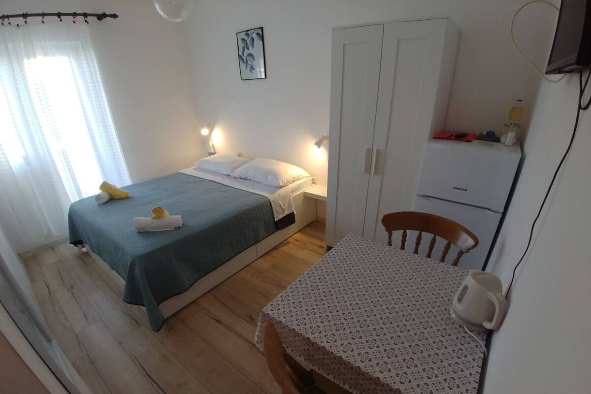 Une chambre comprenant un lit, une table de chevet, une chaise, une armoire et un petit coin cuisine.
