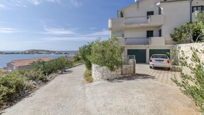 Un bâtiment à deux étages avec une voiture garée dans l’allée, un mur de pierre et une vue sur la mer.