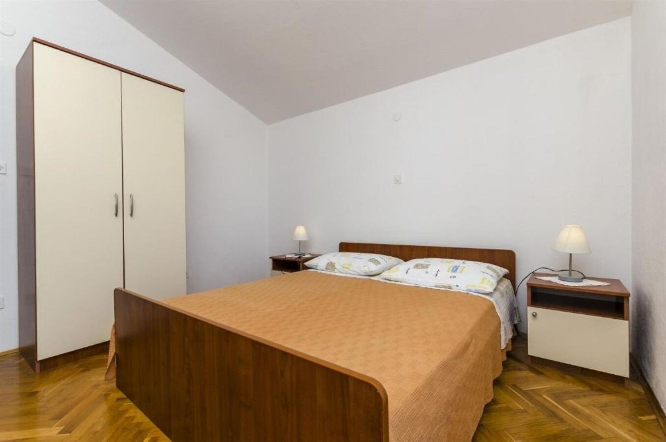 A bedroom with a wooden bed, a wardrobe, a nightstand with a lamp, and a bedside table with a lamp.