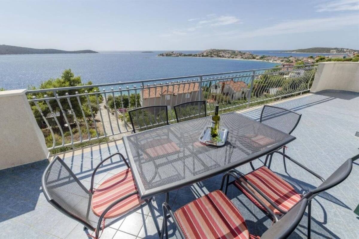 A balcony with a table and chairs, overlooking a coastal view.