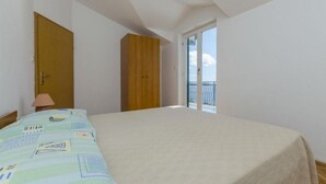 Une chambre à coucher avec un lit, une armoire en bois, une porte et un balcon doté d’une balustrade.