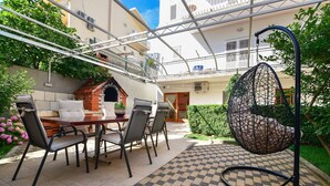 An outdoor patio with a dining table, chairs, a hanging chair, and a brick oven. - Apartment Marijo (Makarska)