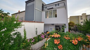 A modern two-story house with a balcony, surrounded by lush greenery and flowering plants. - Apartment Marijo (Makarska)