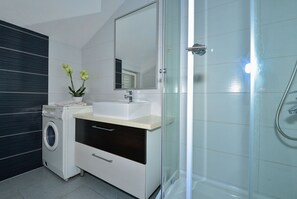 A modern bathroom with a washing machine, a sink, a mirror, and a glass shower enclosure. - Apartment Marijo (Makarska)