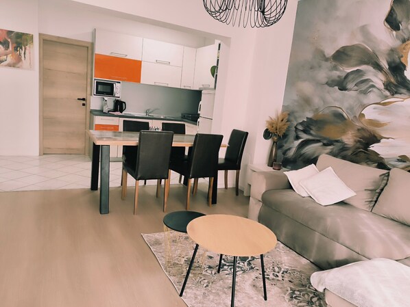 A modern living room with a grey sofa, a small round table, and a dining area with a wooden table and black chairs. - Apartment Marijo (Makarska)