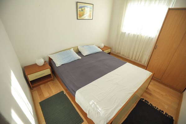 A bedroom with a bed, bedside tables, a nightstand, a framed picture on the wall, and a wardrobe. - Apartments Teo (Privlaka)