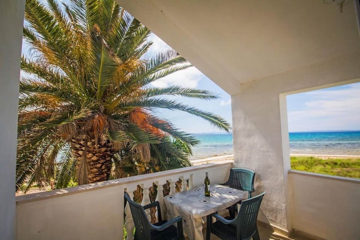 Un balcone con tavolo e sedie, vista su una spiaggia e palme.