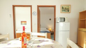 A dining area with a table set for two, a bottle of wine, and glasses. A microwave and a refrigerator are visible in the background. - Apartments Teo (Privlaka)