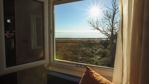 A room with a window overlooking a natural landscape, a bed with a pillow, and a door. - Apartments Teo (Privlaka)