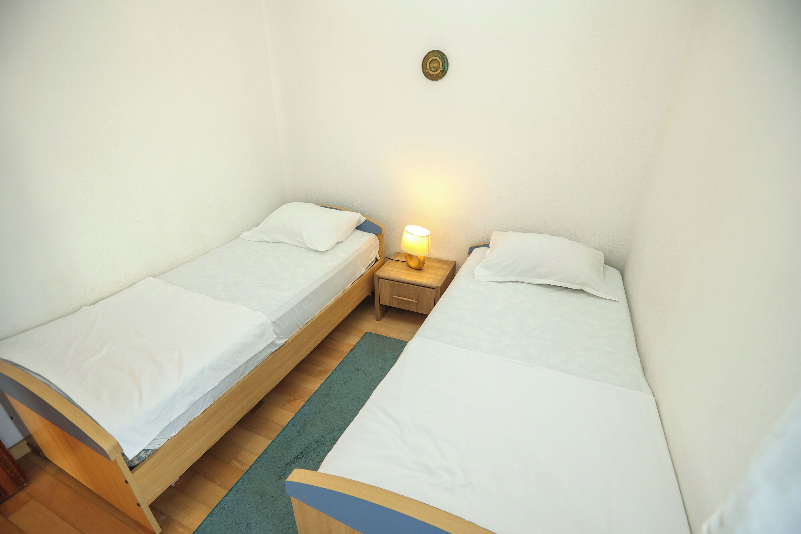 Une petite chambre propre, avec deux lits simples, une table de chevet avec une lampe et un plancher en bois.