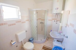 A bathroom with a toilet, shower, sink, and a window. - Apartments Teo (Privlaka)