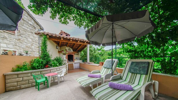 An outdoor patio with two lounge chairs, a small table, and a brick oven. - Apartment Nedjeljka (Postira)