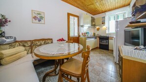 A cozy kitchen with a round table, wooden chairs, a sofa, and a dining table with a lace tablecloth. - Apartment Nedjeljka (Postira)