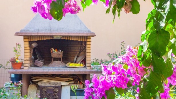 An outdoor brick oven with a chimney, surrounded by potted plants and flowers. - Apartments Tomislava (Makarska)