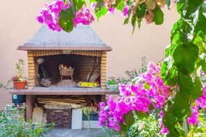 Ein Backofen aus Backsteinen mit Schornstein, umgeben von Blumentöpfen und Blumen.