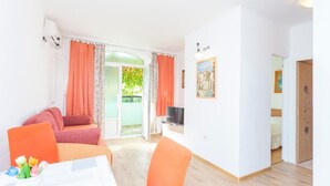 A room with a sofa, a dining table with chairs, a TV, and a door leading to another room. - Apartments Tomislava (Makarska)
