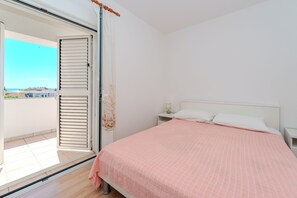 A bedroom with a bed, a nightstand, a window with a view of the outside, and a sliding door to a balcony. - Apartments Mlado (Privlaka)