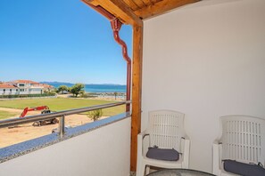 A balcony with two white chairs and a view of a construction site and beach. - Apartments Mlado (Privlaka)