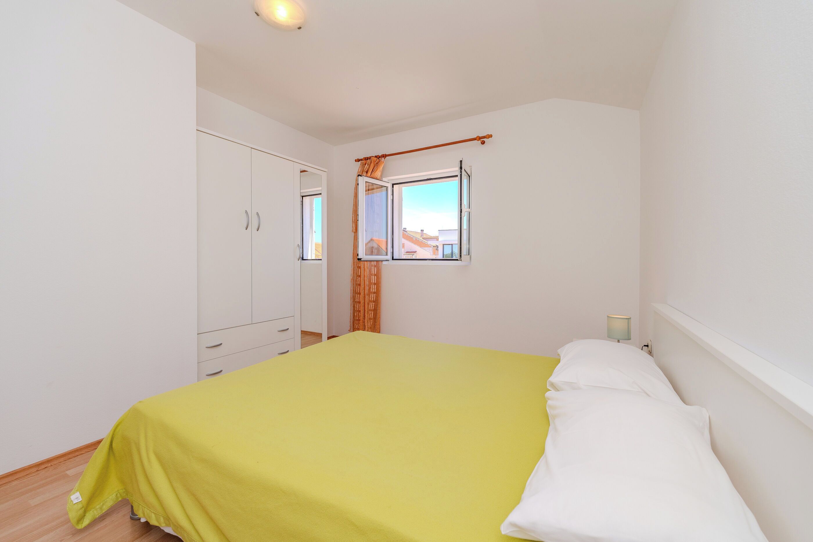 Une chambre à coucher comprenant un lit, une armoire, une fenêtre avec des rideaux et une lampe de chevet.