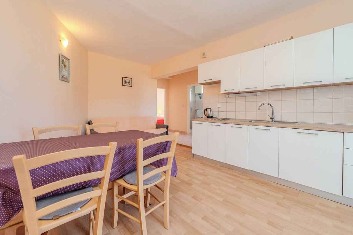 A compact kitchen with white cabinets, a wooden dining table with chairs, and a tiled backsplash.