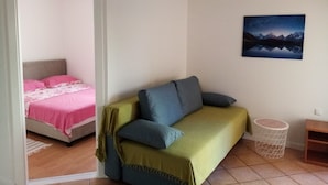 Een kamer met een bed, een bank, een schilderij en een prullenbak.