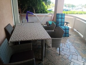 A patio with a table and wicker chairs, a stop sign in the background, and a view of parked cars. - Apartments Sab (Povljana)