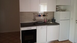 Een compacte keuken met witte kastjes, een inbouwoven, een spoelbak en een koelkast.