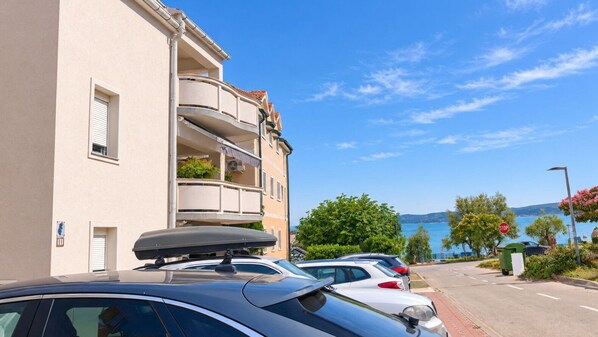 A row of cars parked along a street with a building featuring balconies and a view of the sea. - Apartments Sab (Povljana)