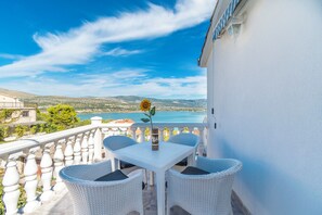 A balcony with a white table and wicker chairs, overlooking a coastal landscape. - Apartment Ivica (Trogir)