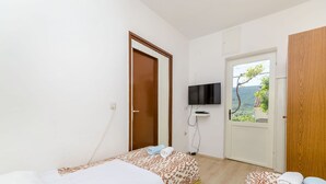 A bedroom with two beds, a TV, and a door leading to a balcony with a view. - Apartment Jasna (Jelsa)