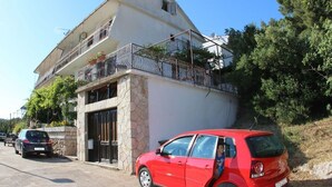 A two-story building with a stone facade, a balcony with metal railings, and a red car parked in front. - Apartment Jasna (Jelsa)